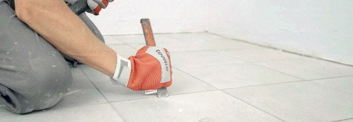 Ein Handwerker entfernt Bodenfliesen mit Hammer und Meisel.